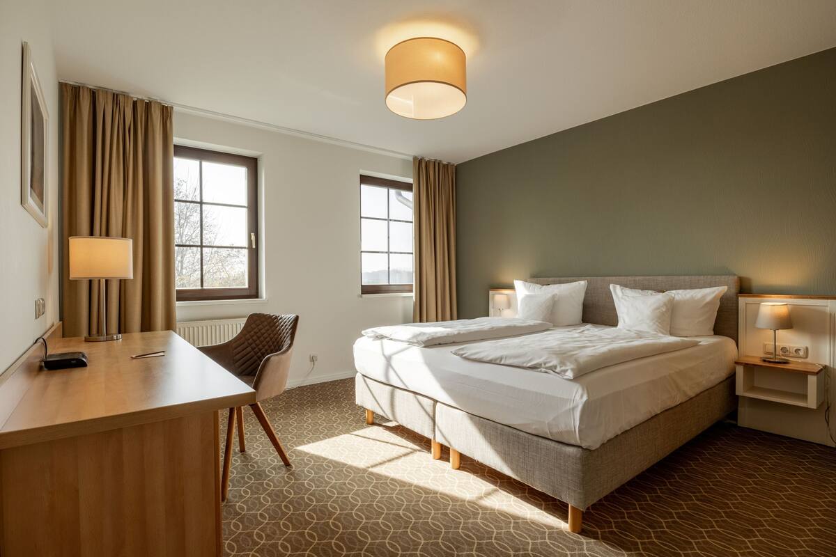 A hotel room with a large bed, a desk, a chair, and two bedside tables with lamps.