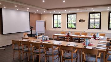 A conference room with wooden tables and chairs, a whiteboard, and windows with plants.