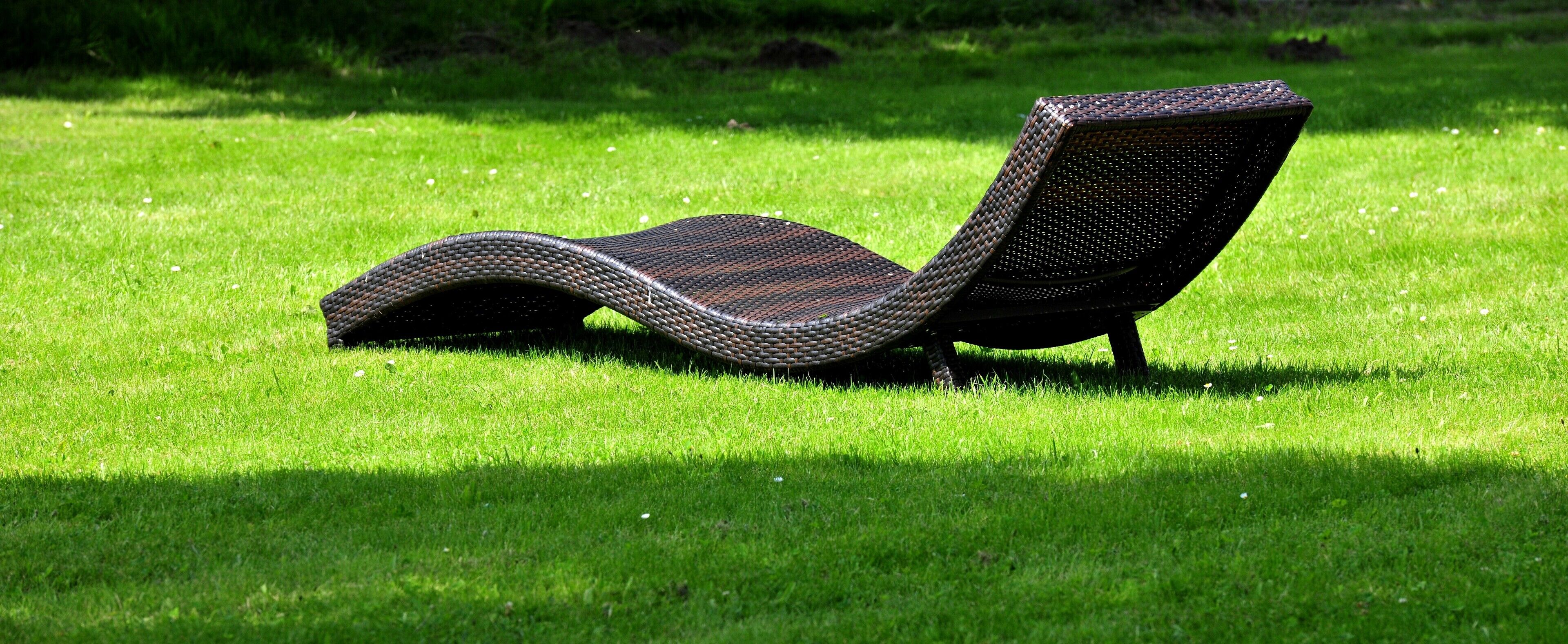 Una silla de salón con asiento y respaldo tejidos, ubicada sobre un césped cuidado.