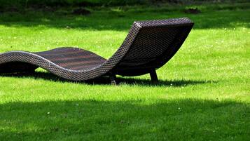 Una silla de salón con asiento y respaldo tejidos, ubicada sobre un césped cuidado.
