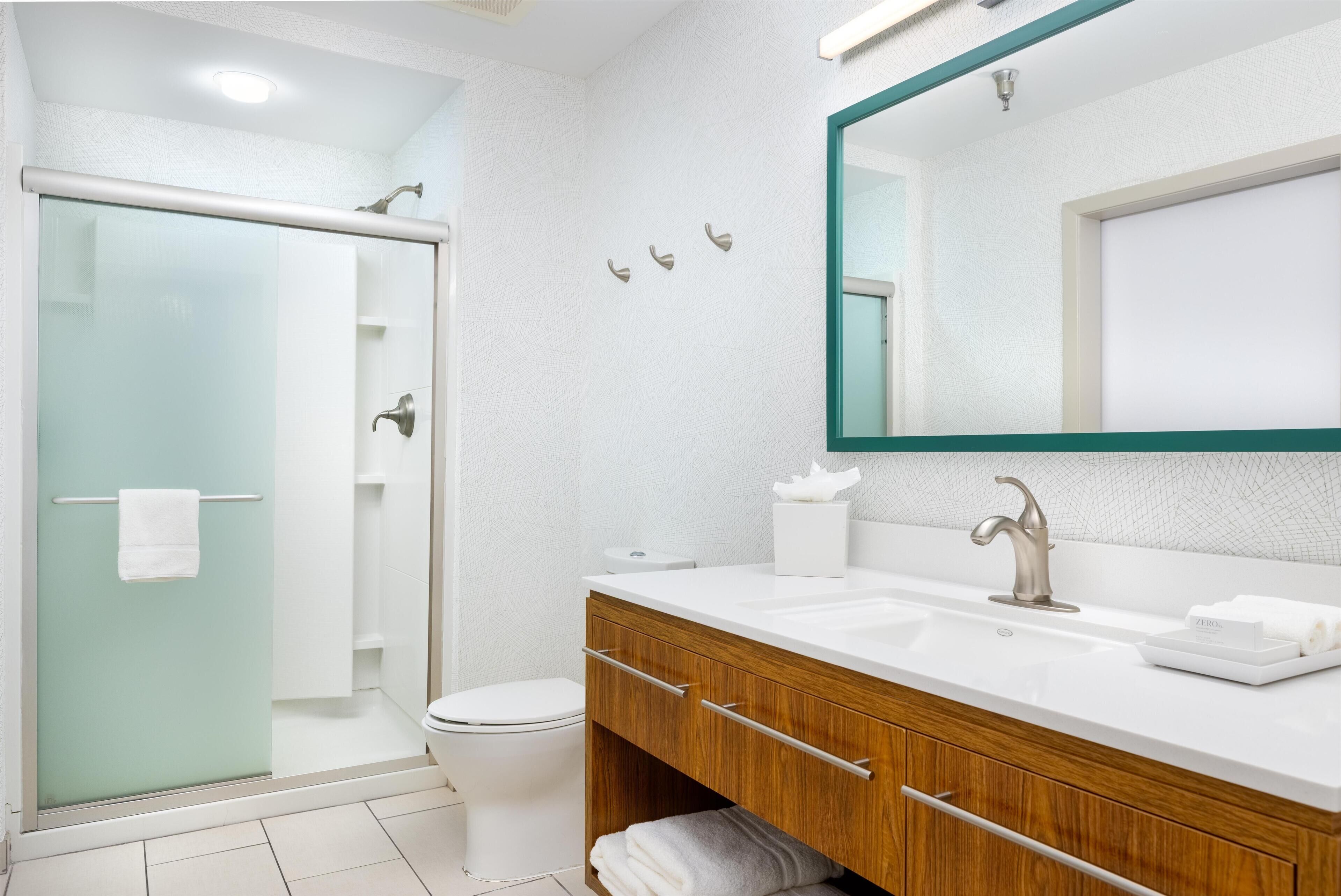 A modern bathroom with a glass shower enclosure, a white sink with a wooden vanity, and a large mirror.