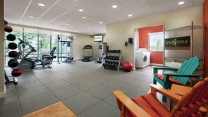 Un gimnasio con equipo de ejercicio, cinta de correr, mancuernas y zona de ciclo indoor.