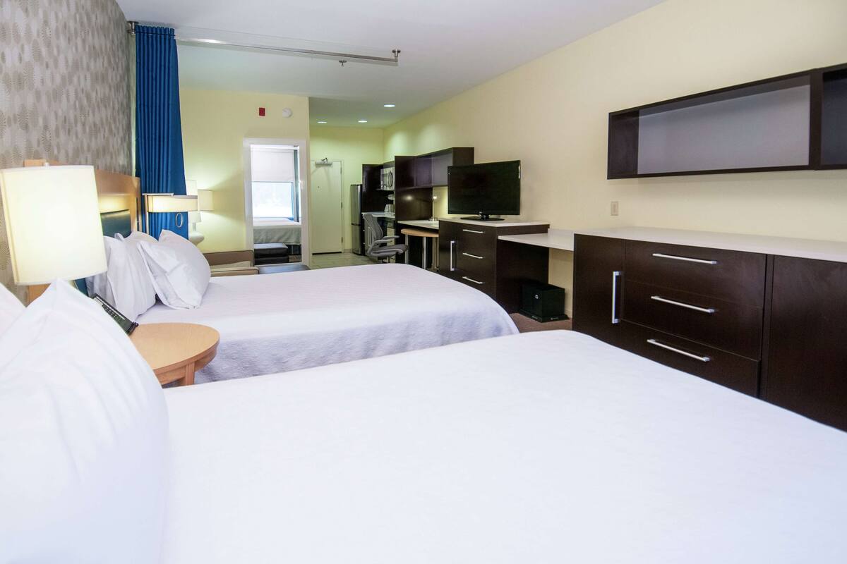 Une chambre d’hôtel avec deux lits, un bureau, une chaise, une télévision et une armoire.