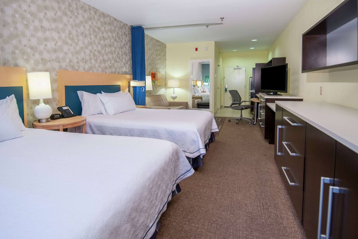 Une chambre d’hôtel avec deux lits, un bureau avec une télévision et une salle de bain visible à travers une porte ouverte.
