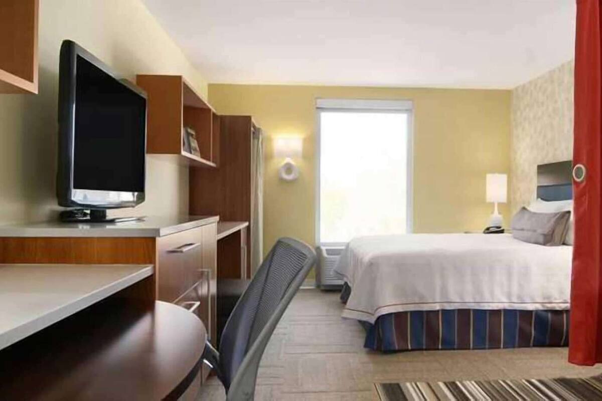 Une chambre d’hôtel comprenant un lit, un bureau avec une télévision, une chaise, un canapé et une fenêtre avec des rideaux.