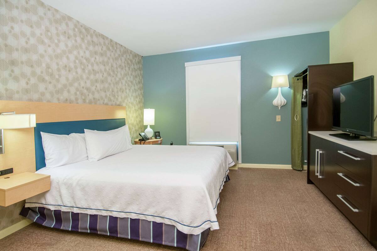 Une chambre d’hôtel avec un grand lit, des tables de chevet, une télévision et une armoire.