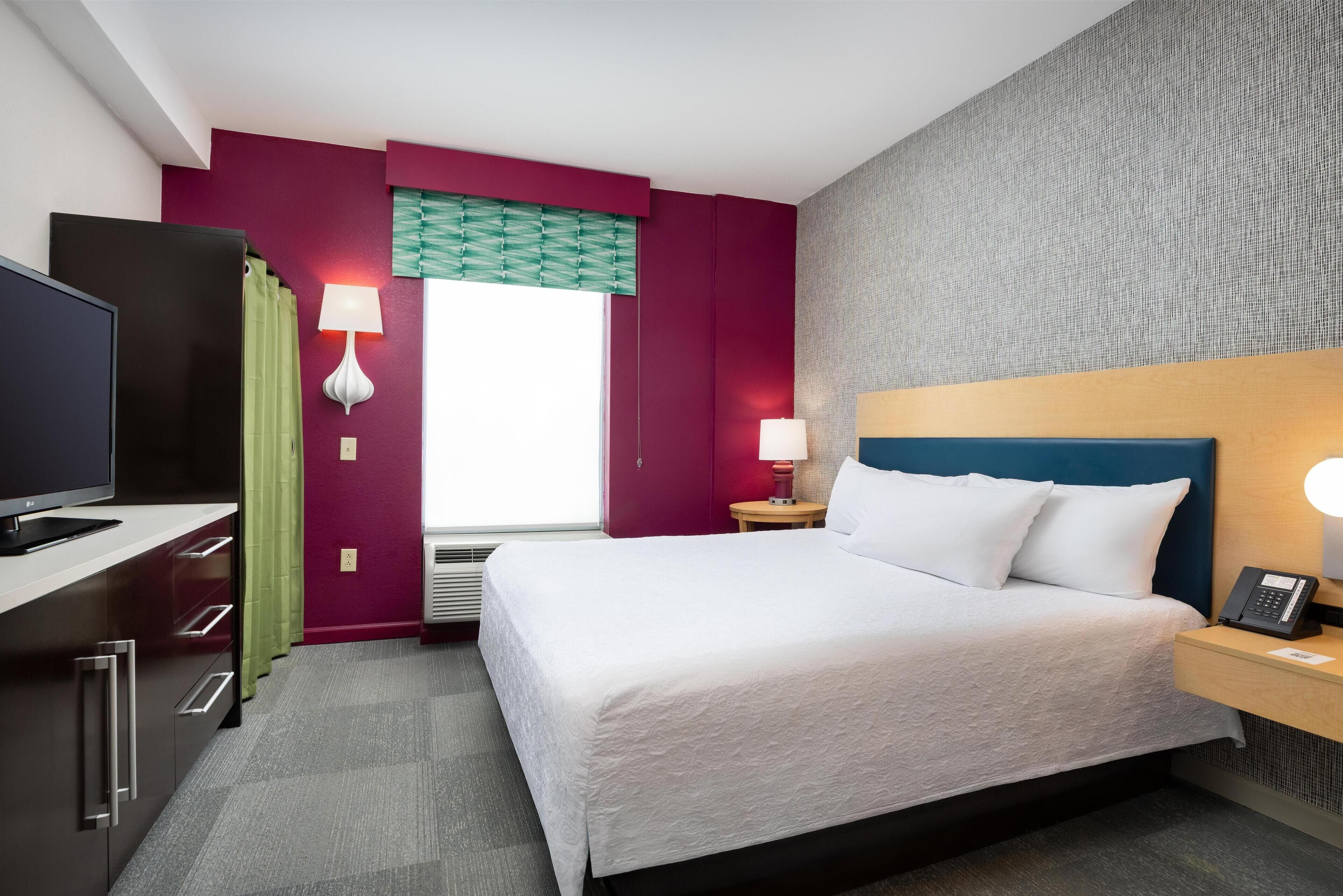 Una habitación de hotel con cama, escritorio, televisor, lámpara y teléfono.