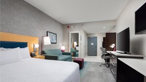 Habitación de hotel con una cama grande, un escritorio, un televisor y una zona de estar con una silla y una mesita.