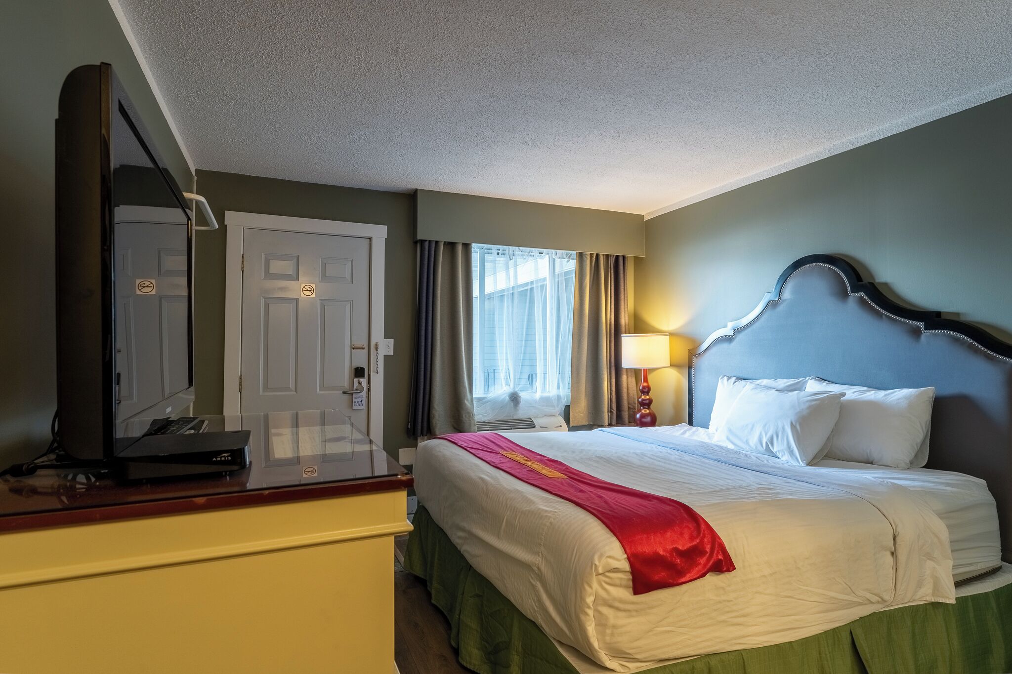 A hotel room with a bed, a desk with a laptop, a television, and a window with curtains.
