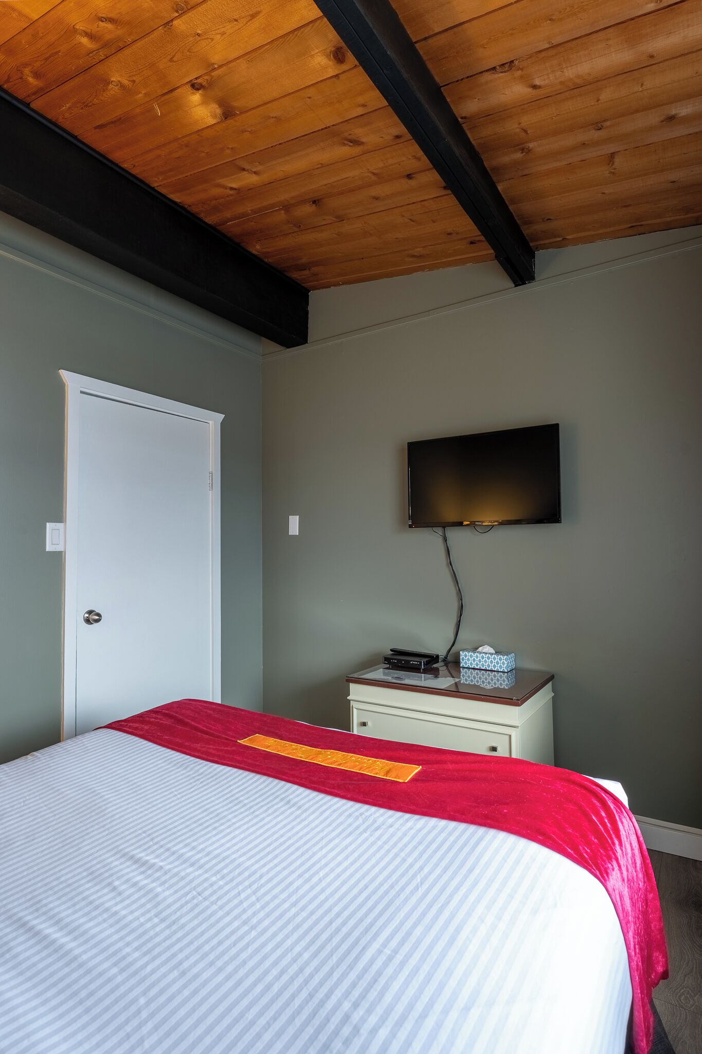 A bedroom with a bed, a television mounted on the wall, a bedside table, and a door.