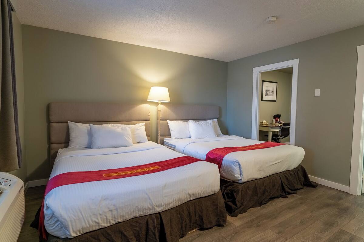 Une chambre d’hôtel avec deux lits, une lampe de chevet, un bureau et une chaise.