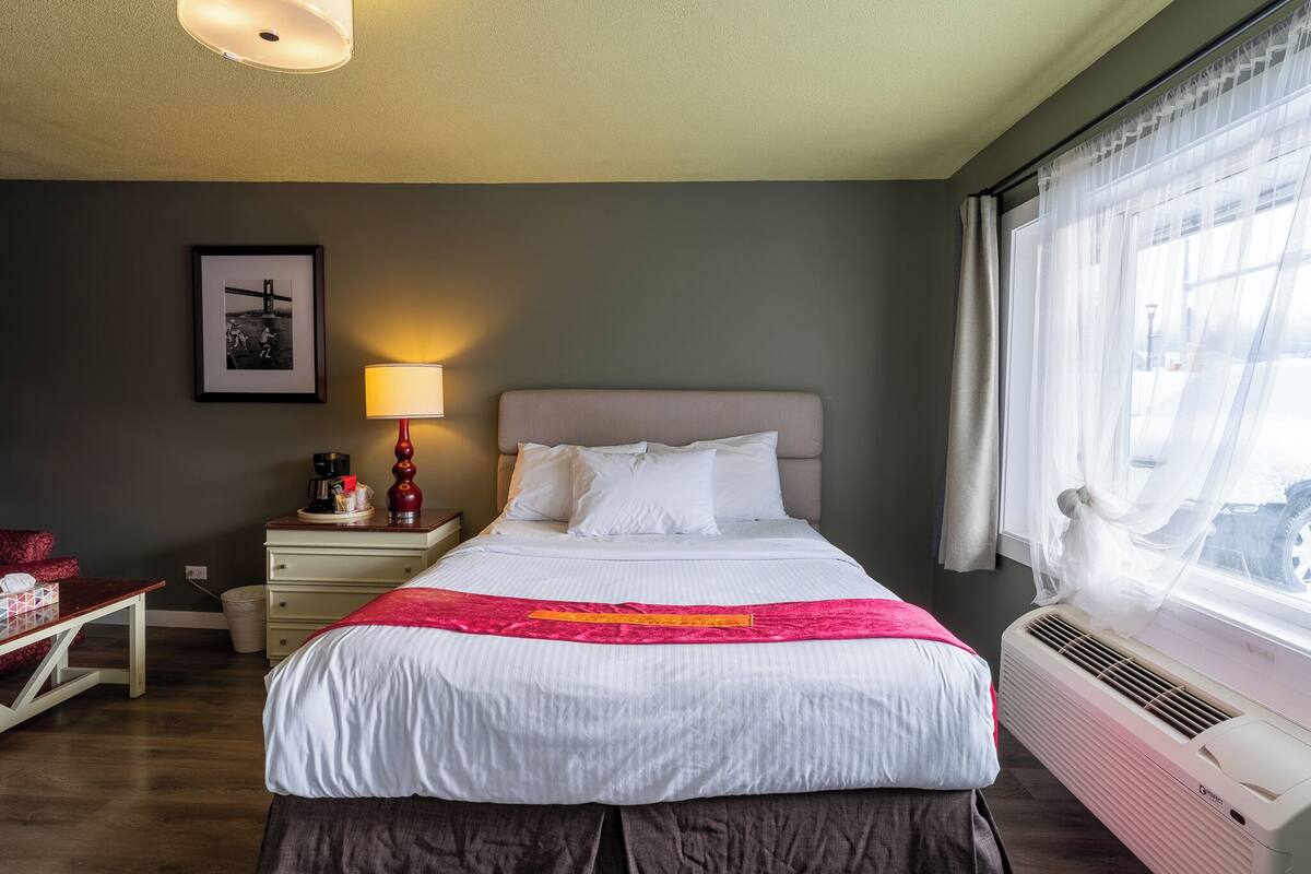 Une chambre d’hôtel bien rangée, avec un lit, une table de chevet, une lampe et un tableau encadré au mur.