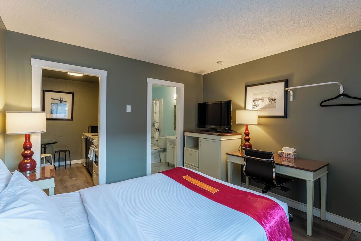 Une chambre d’hôtel avec un lit, un bureau, une télévision et une salle de bain visible à travers une porte ouverte.