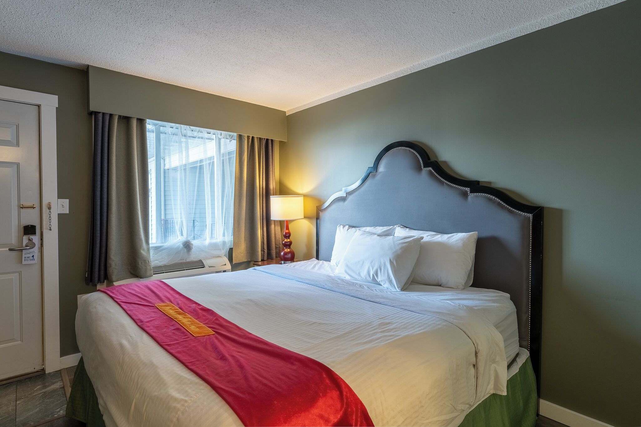 A hotel room with a bed, a nightstand, a lamp, and a window with curtains.