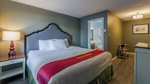 Une chambre d’hôtel avec un grand lit, une table de chevet avec une lampe, une commode et un tableau encadré au mur.