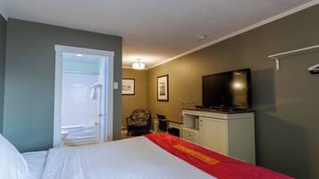 Habitación de hotel con cama, escritorio, silla, televisión y baño visible a través de una puerta abierta.