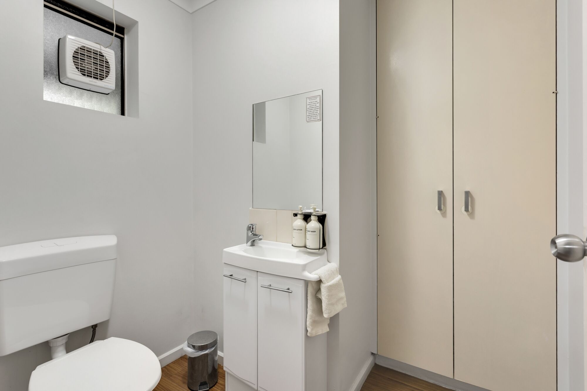 A bathroom with a toilet, sink, mirror, and storage cabinet.