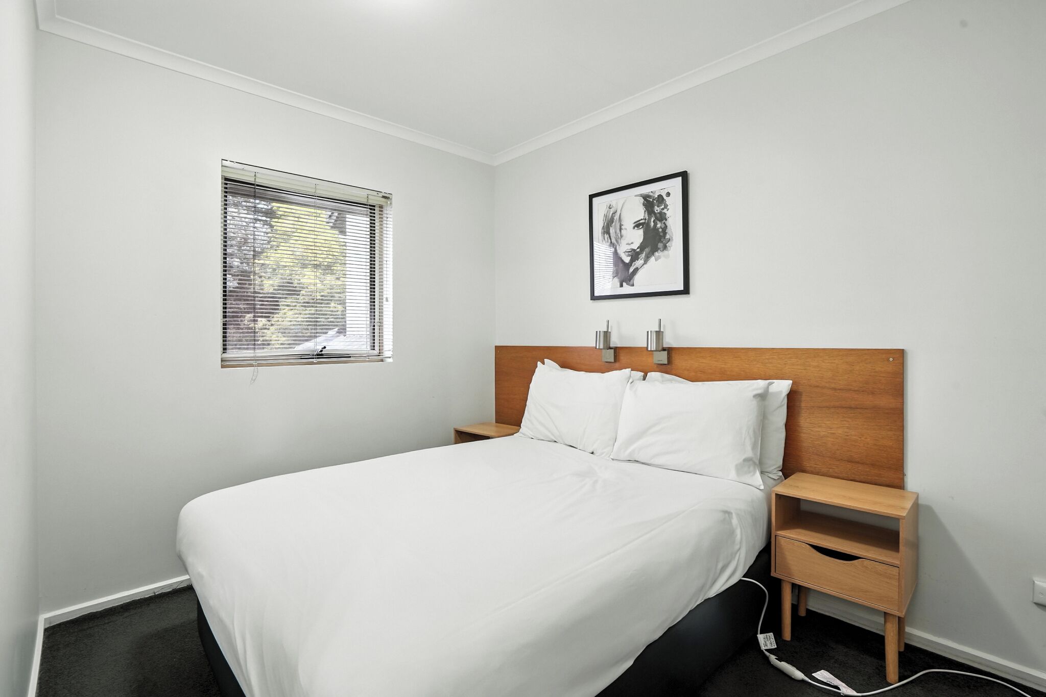 A neatly made bed with white linens, a wooden headboard, and a nightstand with a drawer.