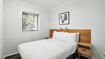 A neatly made bed with white linens, a wooden headboard, and a nightstand with a drawer.