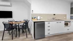 A compact kitchen with a dishwasher, a sink, and a microwave. There is a dining area with a table and chairs. - Elphin Motel & Serviced Apartments (Launceston)