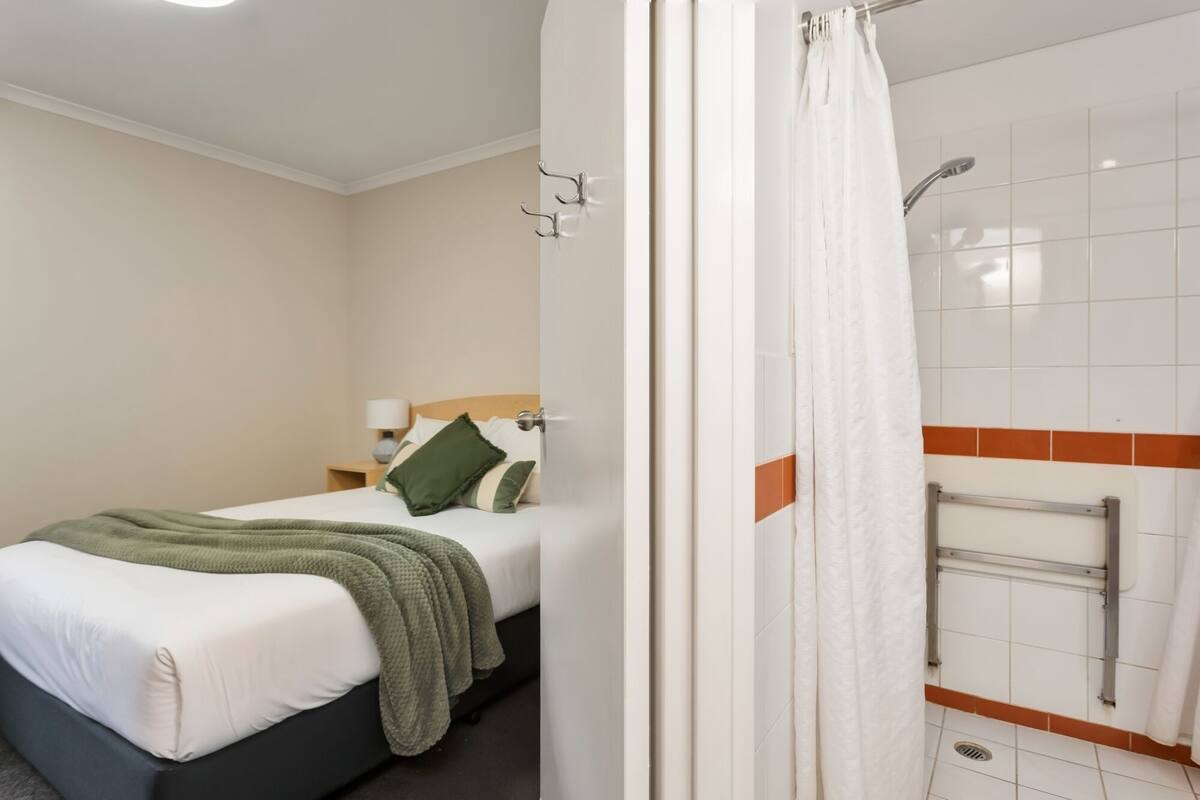 A hotel room with a bed, a nightstand, a shower with a towel rack, and a curtain.