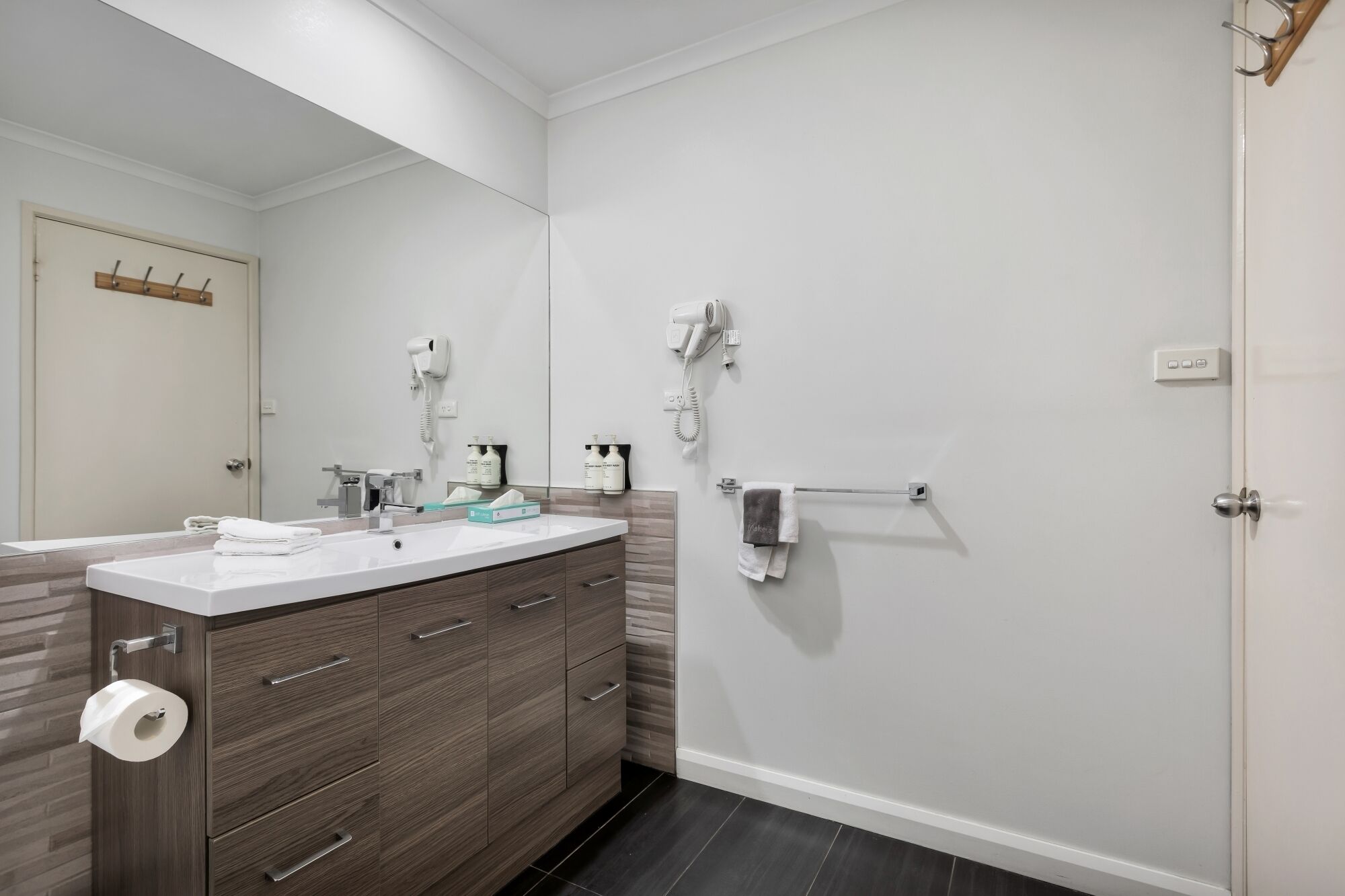 Un baño moderno con un espejo grande, dos lavabos, un secador de pelo y un perchero para toallas.