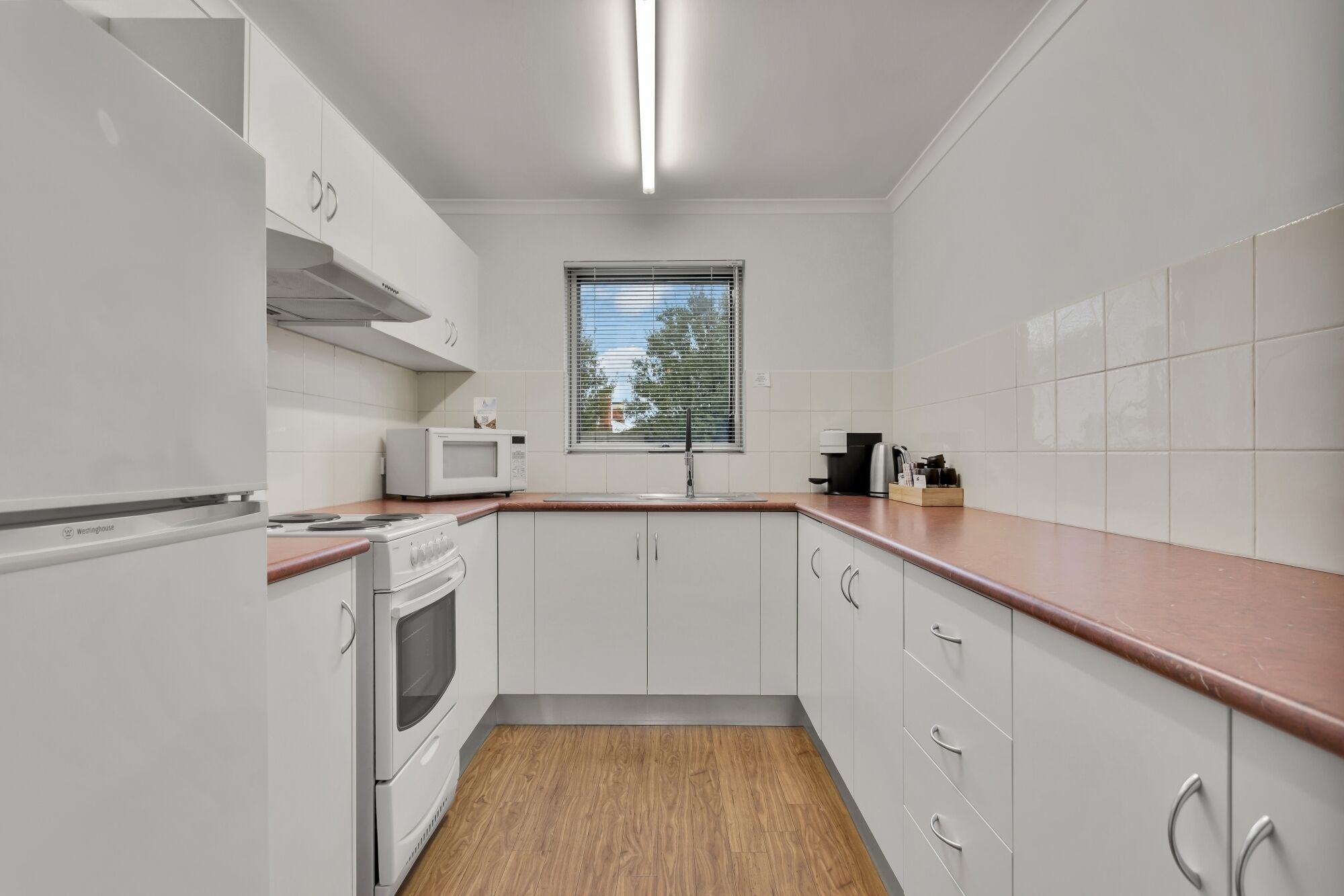 A modern kitchen with white cabinets, a microwave, a stove, and a window with blinds.