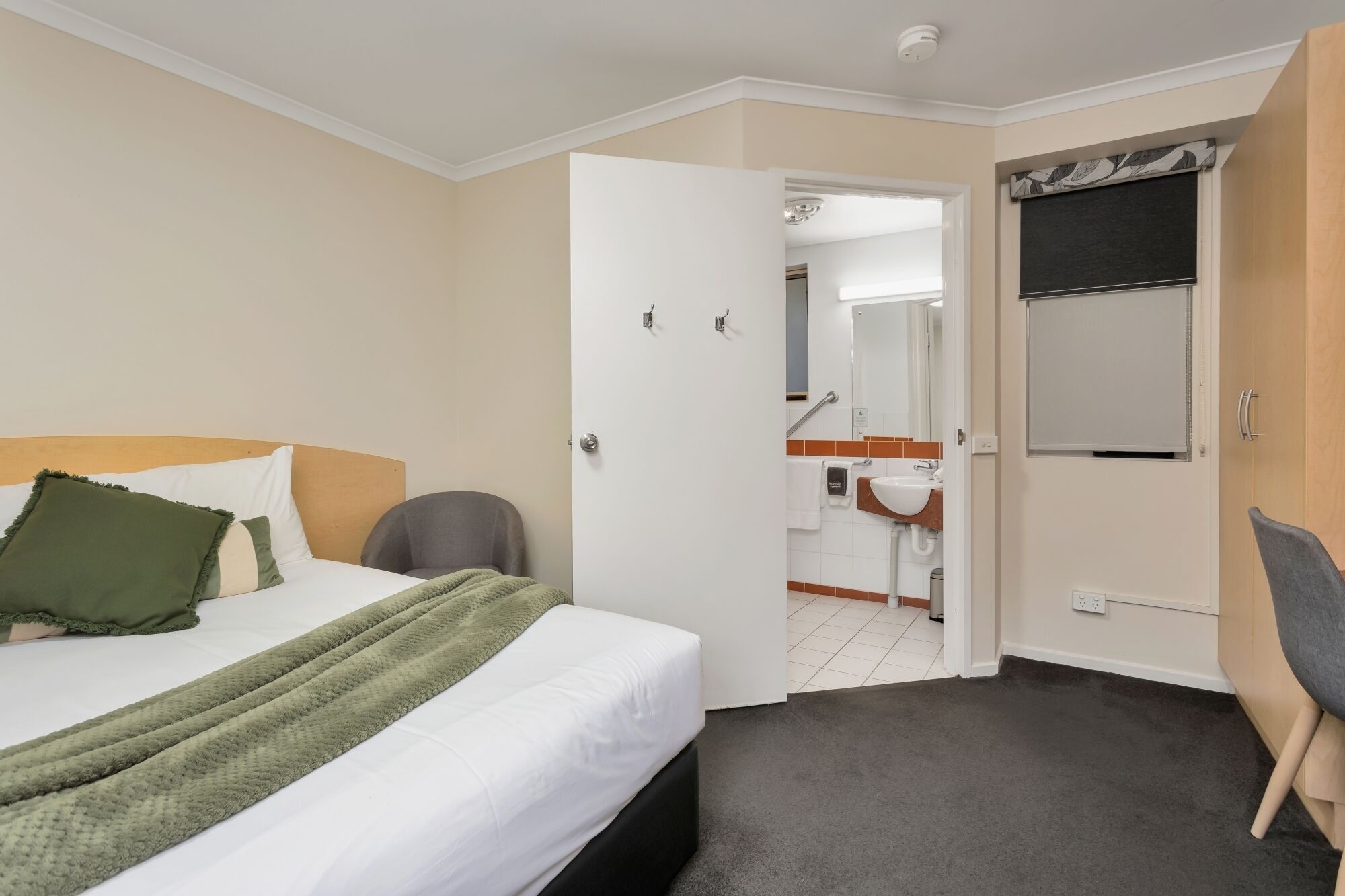 A hotel room with a bed, a chair, a desk, and a bathroom visible through an open door.