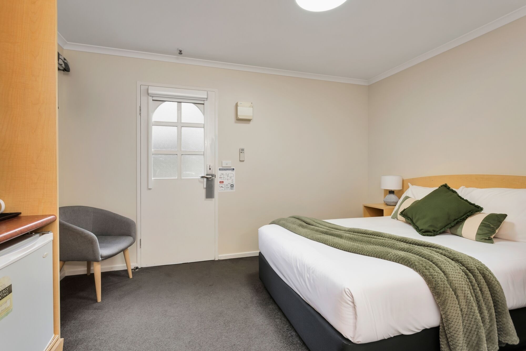 Quarto de hotel com cama, escrivaninha, cadeira, janela e porta.