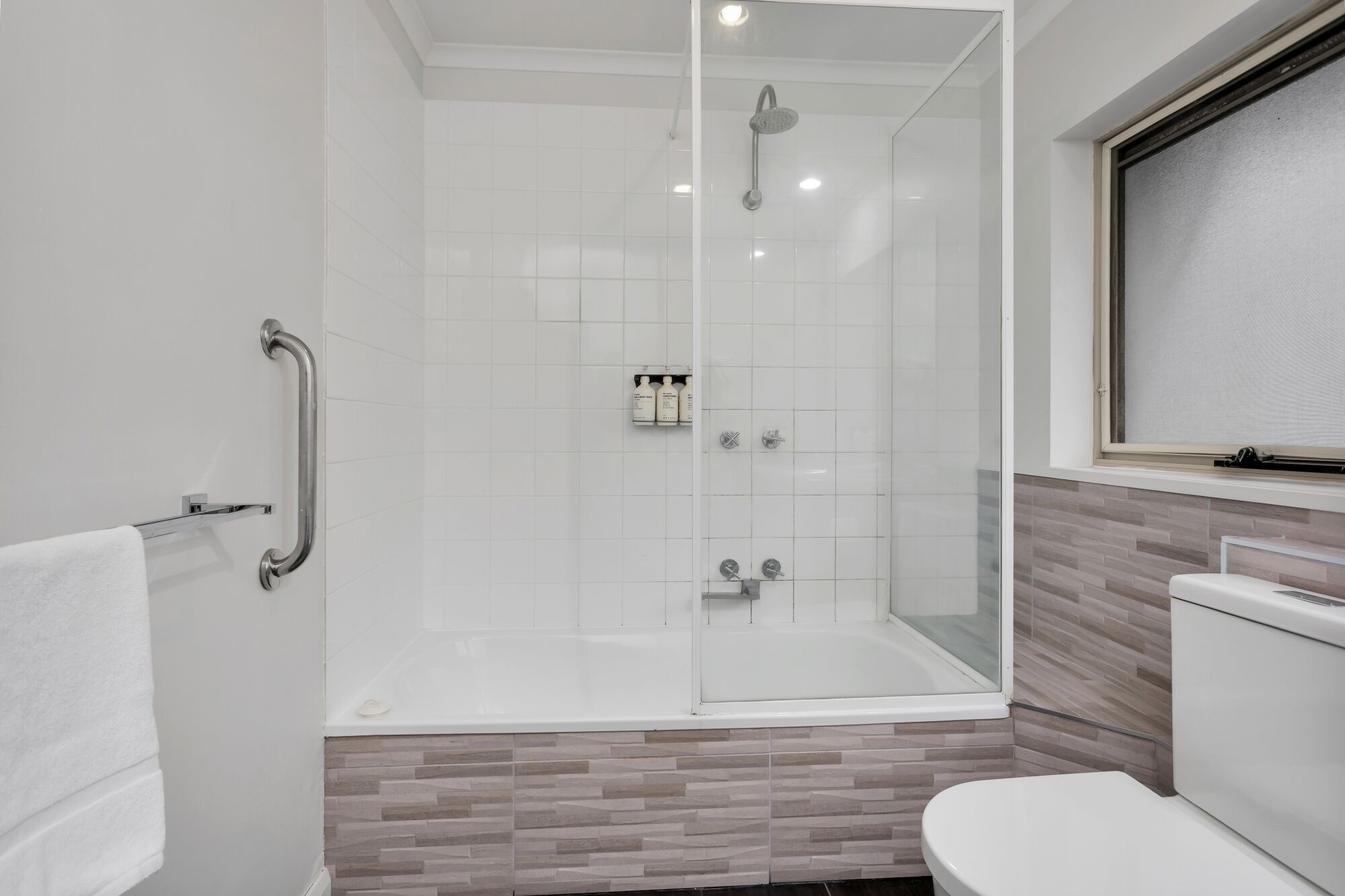 Un baño moderno con ducha de vidrio, inodoro blanco y tocador de madera.