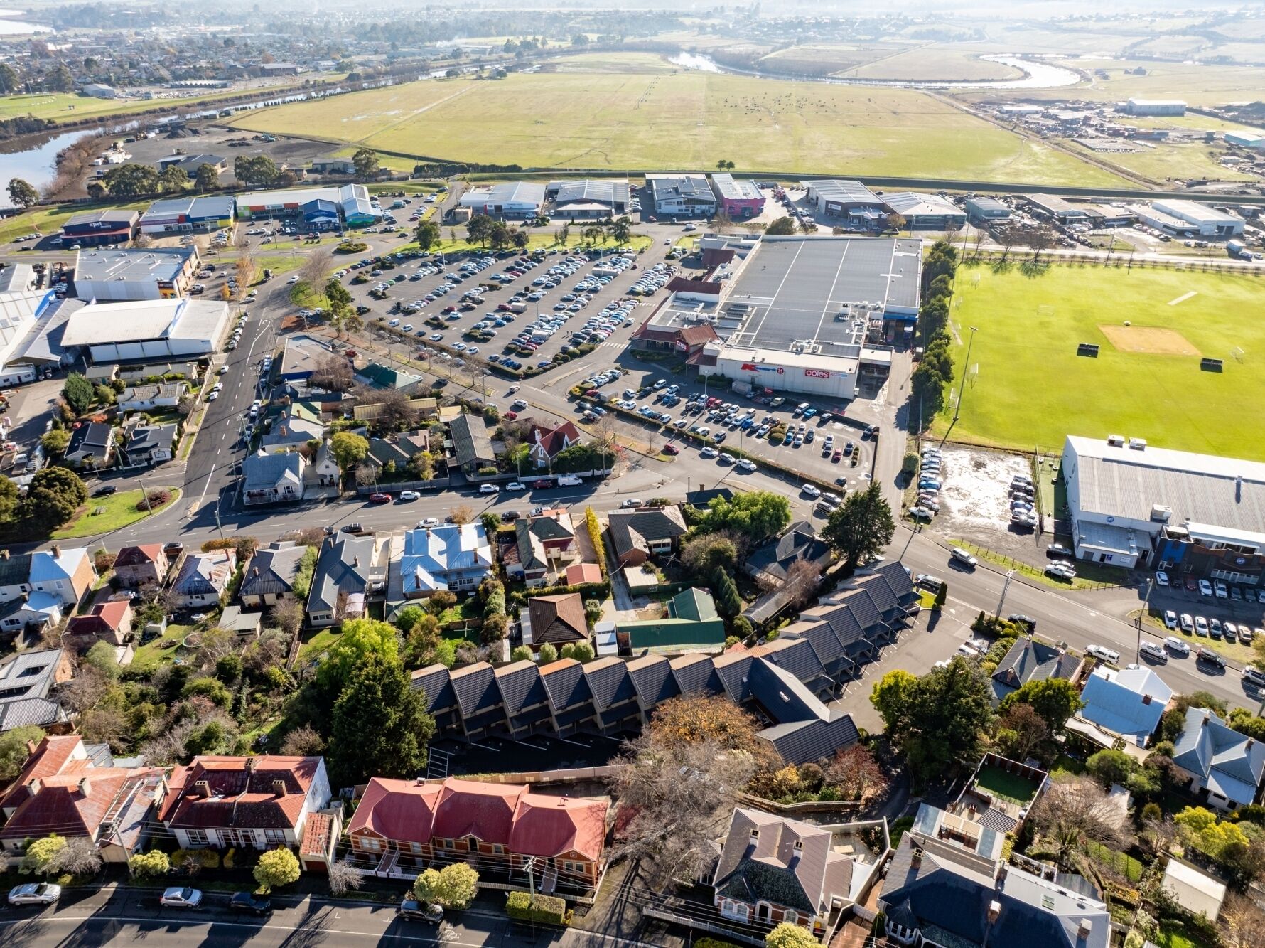 Vue aérienne d’une zone commerciale comprenant un grand parking, plusieurs bâtiments et un terrain de sport.