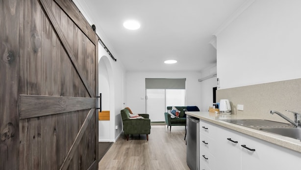 A modern kitchen with white cabinets, a stainless steel sink, and a wooden door. - Elphin Motel & Serviced Apartments (Launceston)