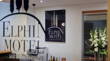A reception desk with a coffee machine, a poster for Elphin Motel, and a window with blinds.