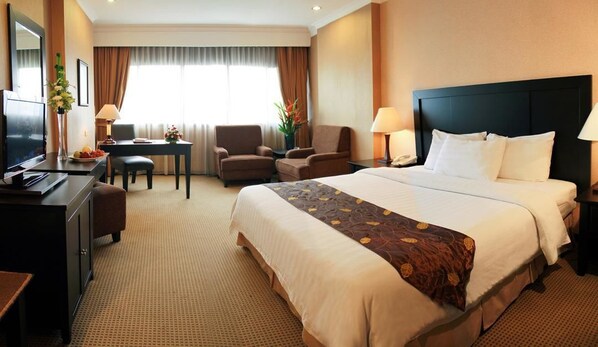 A hotel room with a large bed, a desk with a chair, a television, and a window with curtains. - Hotel Danau Toba International (Medan)