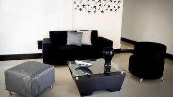 Una sala de estar moderna con un sofá negro, una mesa de centro de vidrio, un otoman gris y un sillón negro.