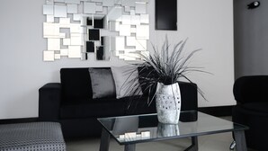 A modern living room with a black sofa, a glass coffee table, and a decorative mirror on the wall. - Hotel El Portón de San Joaquín (Medellín)