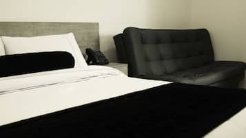 Een hotelkamer met een bed, een zwarte leren fauteuil en een telefoon op het nachtkastje.