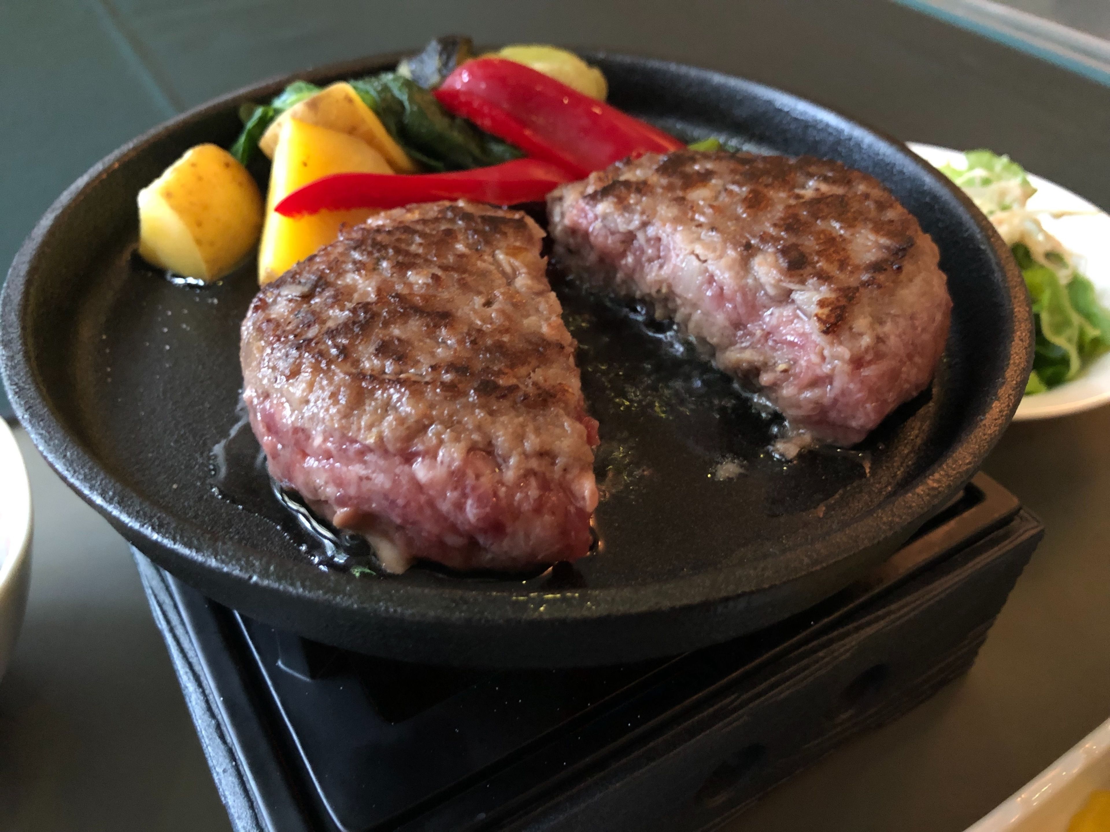 A pan with two pieces of meat and vegetables on a stove.