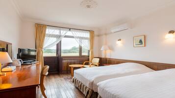A hotel room with two beds, a desk with a lamp, a television, a chair, and a window with curtains.