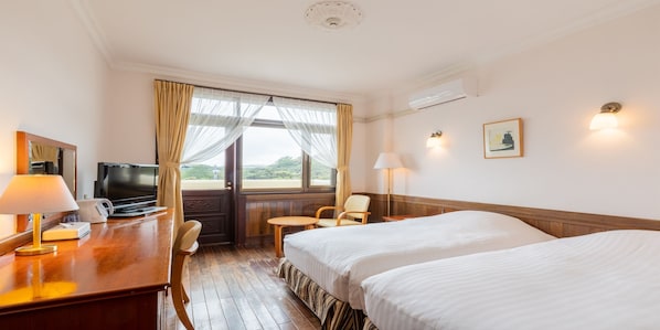Habitación de hotel con dos camas, un escritorio con lámpara, televisión, una silla y una ventana con cortinas.