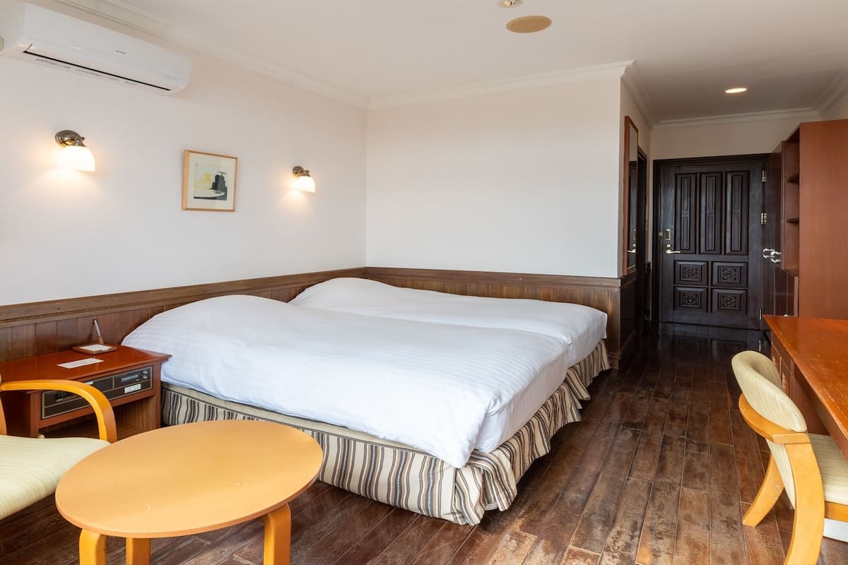 Hotellihuone, jossa on suuri sänky, kaksi yöpöytää, työpöytä tuolilla, pieni pyöreä pöytä ja puinen penkki.