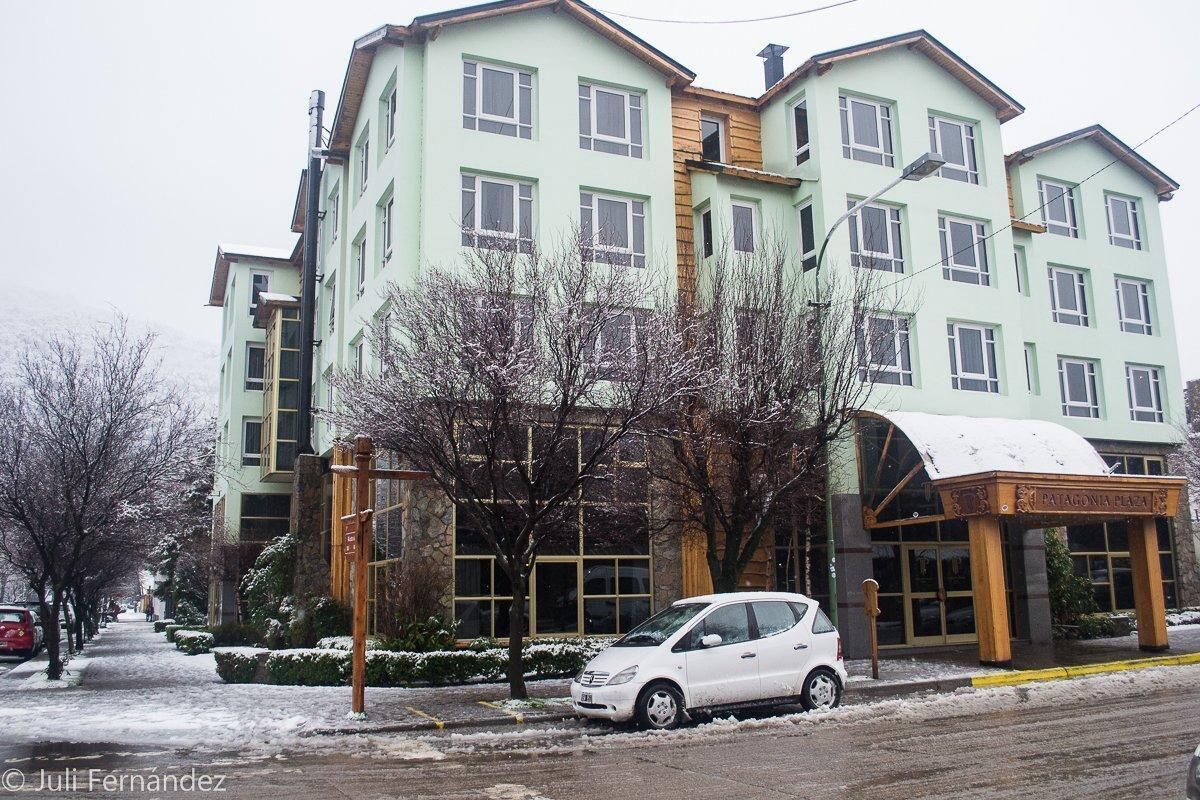 Un hotel de varios pisos con fachada verde claro, un acceso cubierto y una calle cubierta de nieve.