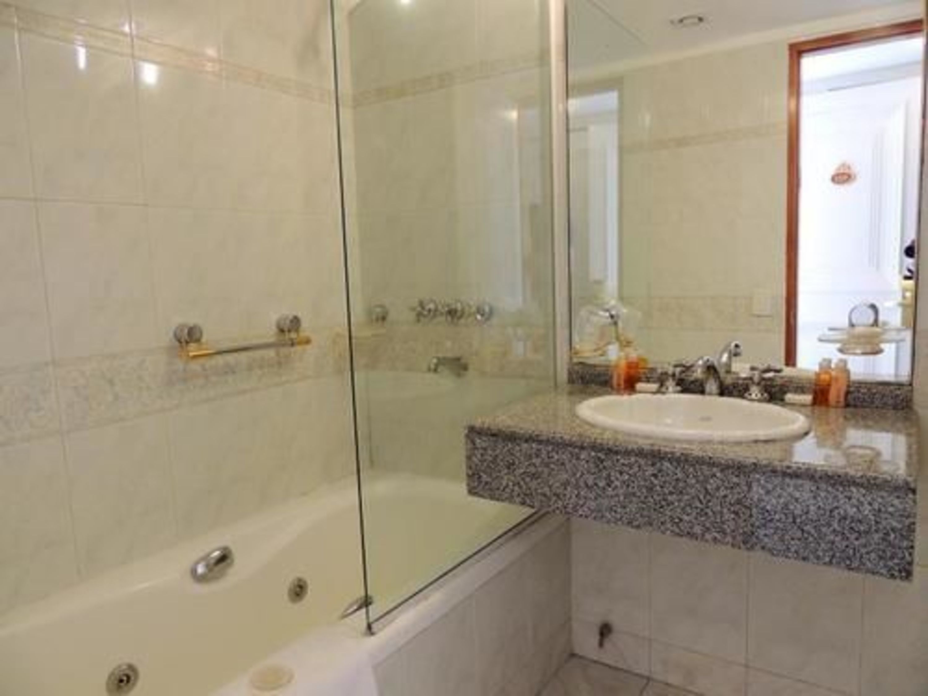 Une salle de bain avec une douche à parois de verre, un lavabo doté d’un plan de travail en granit et un miroir.