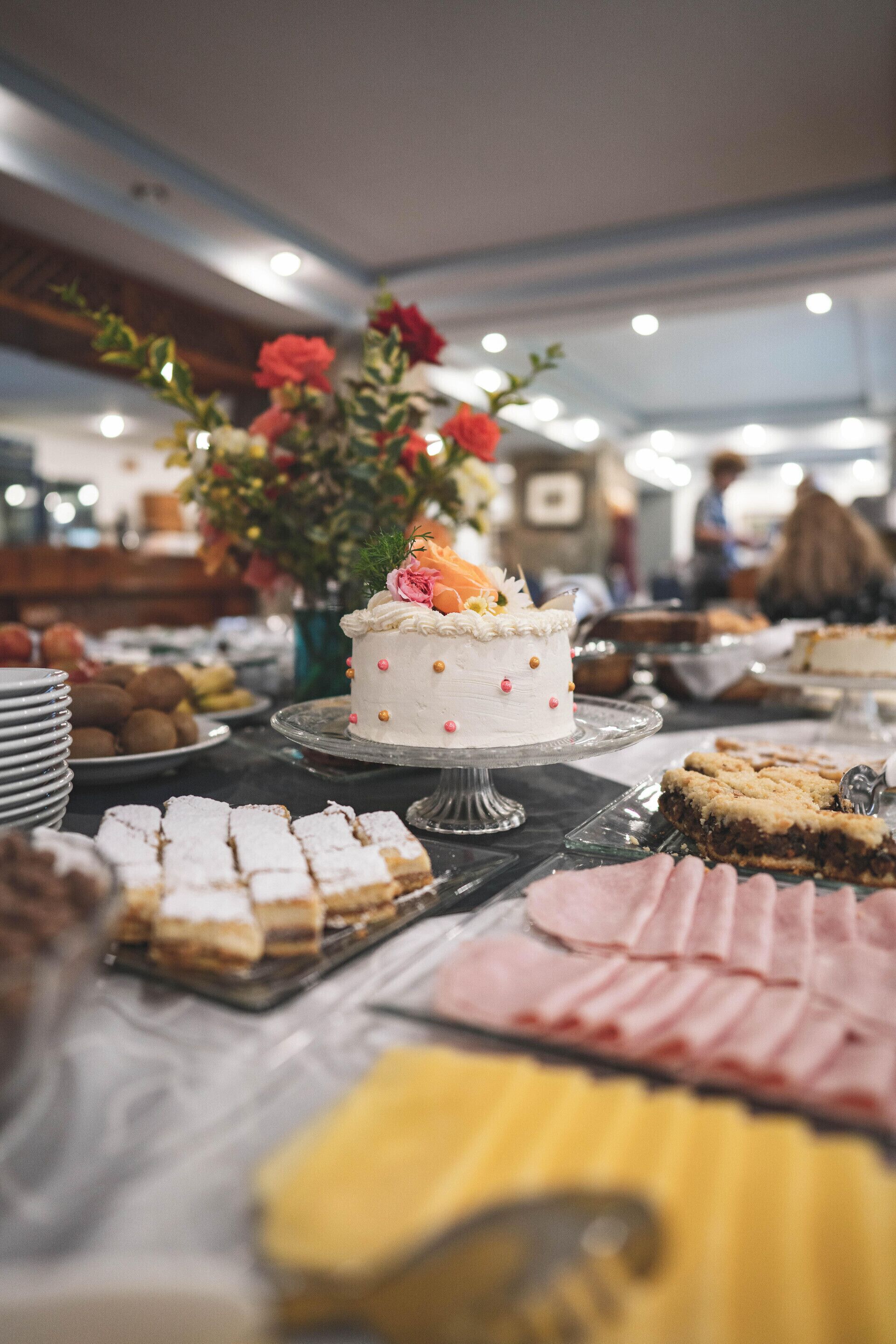 Uma mesa de buffet com diversos doces, incluindo um bolo decorado e variedade de pastelaria.