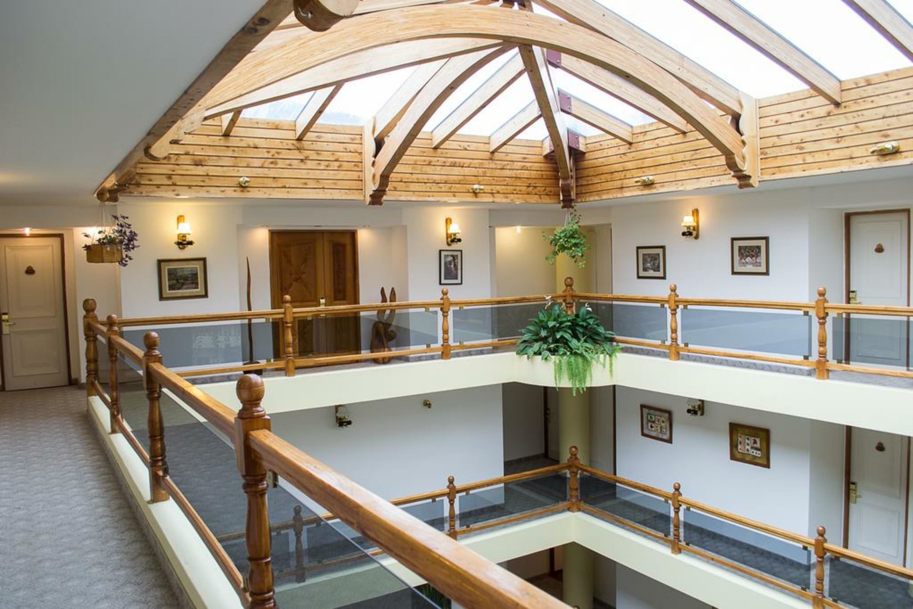 A multi-level interior with wooden railings, a glass balustrade, and a central hanging plant.