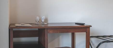 A compact room with a wooden desk, a small black refrigerator, a stool, a wall-mounted TV, and a wall-mounted air conditioner.