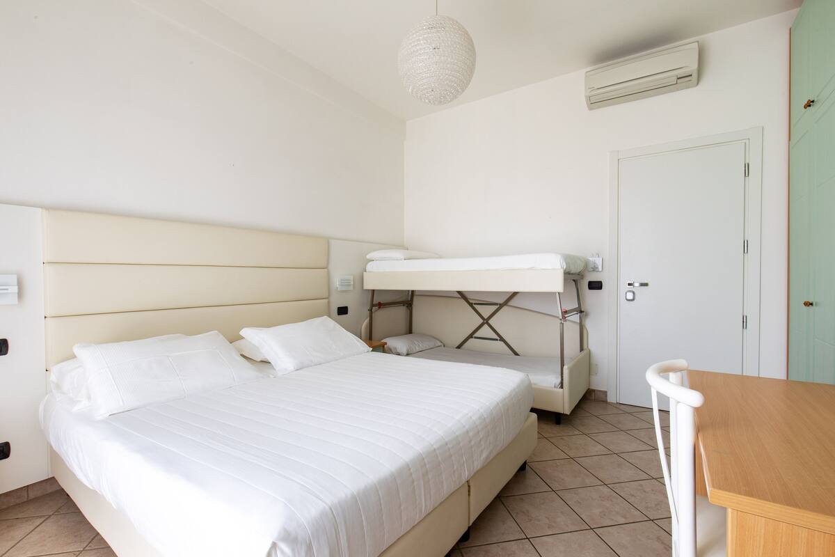 Una camera da letto con un letto grande, un letto a castello, un tavolo in legno e una lampada a sospensione.