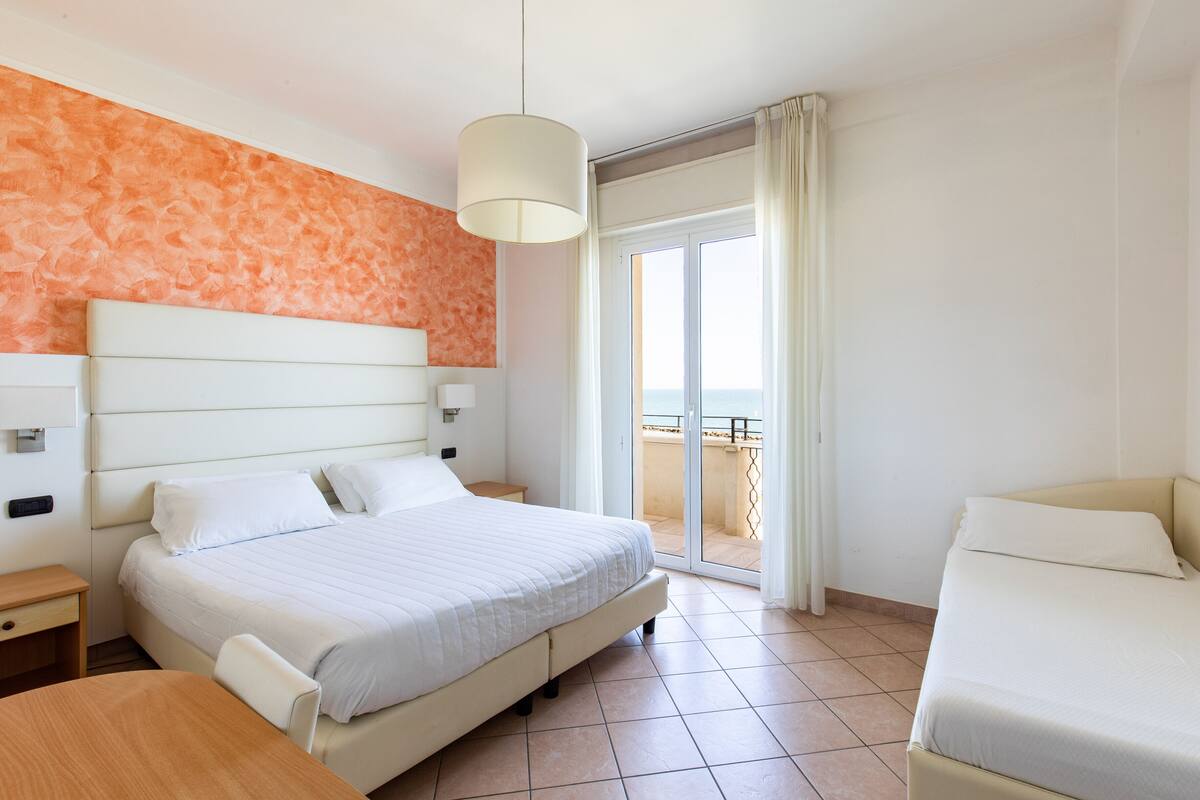 Camera d'albergo con un letto grande, un letto più piccolo, una scrivania e un balcone con vista.
