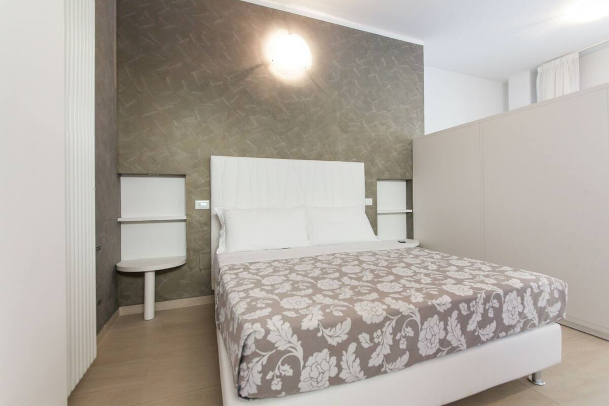 Una camera da letto con un letto, due comodini, una lampada a parete e un armadio.