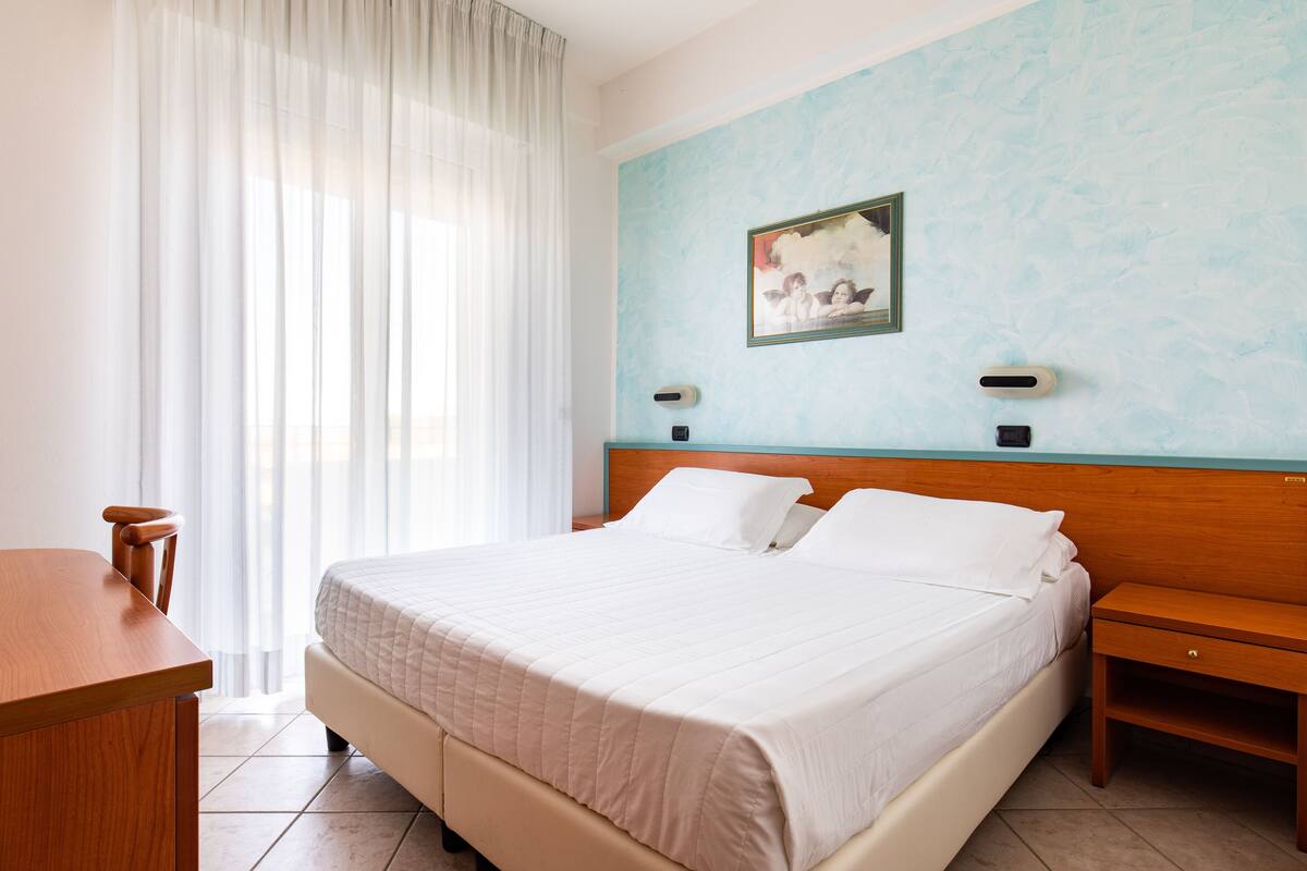 Una camera d'albergo con un letto, un comodino in legno, una scrivania e un quadro appeso al muro.